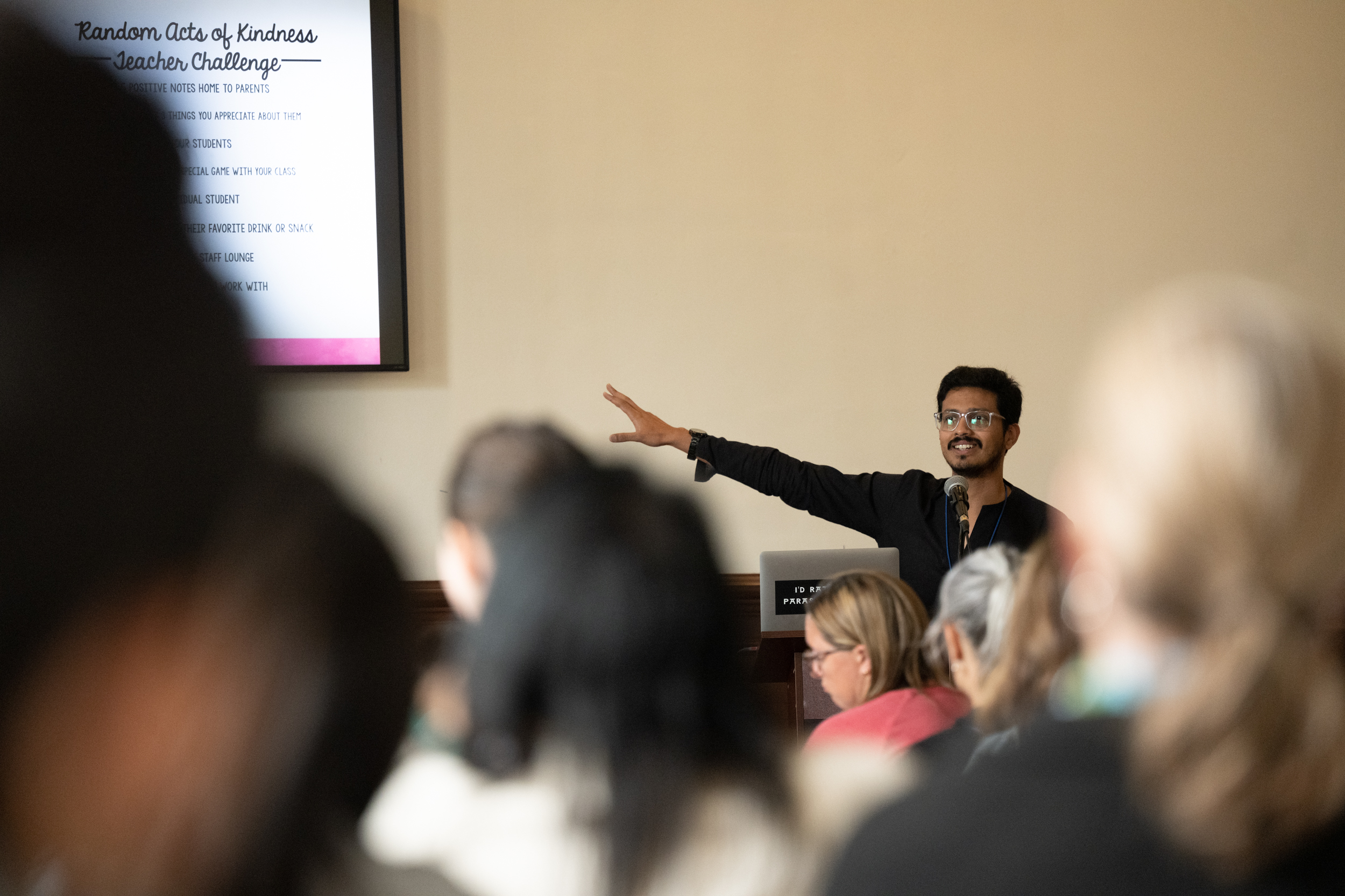 Image of Aakash Chowkase conducting a teachers' workshop. He can be seen pointing at the screen in the front of the class with a bright smile on his face. He is wearing transparent glasses.
